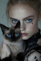 Young woman with freckles and striking blue eyes holds Siamese cat with matching blue eyes, both gazing intensely at camera. Black lace and delicate butterfly detail create ethereal mood.