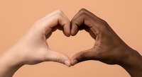 Two diverse hands forming heart shape symbol representing unity love friendship and racial harmony against warm beige background for social campaigns.