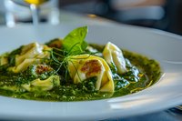 Fresh tortellini pasta in vibrant basil pesto sauce garnished with microgreens and parmesan on white plate, close-up view of gourmet Italian cuisine.