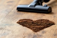 Heart shape made from coffee grounds on wooden surface with vacuum cleaner nozzle, representing cleaning and coffee passion concept.
