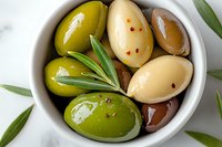 Mixed marinated olives with garlic and herbs in white ceramic bowl, close up view. Fresh olive leaves and peppercorns add natural garnish. Mediterranean appetizer.