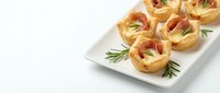 Elegant puff pastry appetizers with prosciutto and herbs served on white plate, perfect for catering events, holiday parties, and gourmet entertaining occasions.