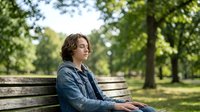 Young woman with curly hair relaxing on park bench in peaceful green outdoor setting, enjoying quiet moment of mindfulness and tranquility in nature.
