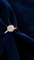 Elegant diamond solitaire engagement ring on luxurious navy blue velvet fabric background for jewelry advertising and wedding proposals.