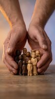 Protective hands sheltering wooden family figures representing care, security and community support in warm lighting for insurance and social concepts.