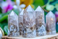 Clear quartz crystal points with smoky inclusions arranged on wooden slice against blurred floral background, showcasing natural mineral formations and healing stones.