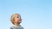 Blonde toddler boy looking upward against clear blue sky, wearing knit sweater. Suitable for parenting, childhood, and lifestyle content.