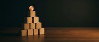 Wooden blocks stacked in pyramid formation with human figure icon on top representing leadership, hierarchy, and business success on dark background.