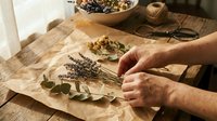 Hands arranging dried herbs and botanicals on kraft paper for herbal tea blending, natural wellness preparation, and aromatherapy crafting on wooden surface.