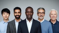 Diverse group of five professional businessmen of different ethnicities and ages standing together in business attire against neutral background.