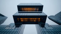Modern office building exterior with geometric black facade and glowing orange windows viewed from below against cloudy sky, showcasing contemporary architecture.