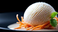 Creamy vanilla ice cream scoop garnished with fresh julienned carrots and mint leaf on dark plate, dramatic side lighting creates appetizing food composition.
