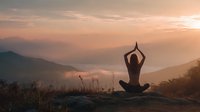 Woman practicing yoga meditation pose on mountain summit at golden sunrise with peaceful valley landscape below.