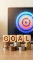 Wooden blocks spelling GOAL on stacked coins with colorful target on computer screen background representing financial planning and achievement strategies.