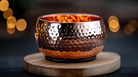 Hammered copper bowl with warm candlelight on wooden board against dark background with golden bokeh lights creates cozy ambiance.