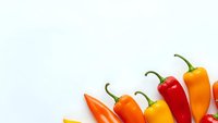 Colorful hot chili peppers arranged in row on white background, isolated spicy vegetables for cooking and culinary design projects.