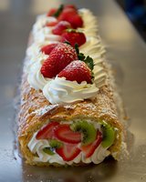Fresh strawberry and kiwi fruit roll cake with whipped cream filling and powdered sugar dusting, decorated with whole berries on dark surface.