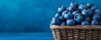 Fresh ripe blueberries in woven basket against blue background with copy space, panoramic format for food and healthy eating concept.