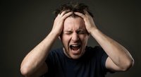 Stressed Caucasian man screaming with hands on head expressing intense frustration and mental pressure against dark background for wellness concepts.