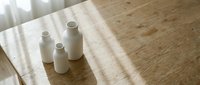 Three white ceramic bottles arranged on natural linen fabric with soft sunlight casting shadows, suitable for cosmetics, skincare, or wellness product mockups.