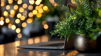 Festive dining table setting with evergreen branches in black vase against warm bokeh lights background creates cozy holiday atmosphere for winter celebrations.