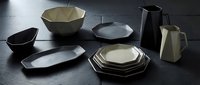 Modern geometric tableware collection with angular bowls, plates and serving pieces in matte black and cream finishes on dark surface for contemporary dining.