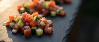 Fresh diced vegetables including tomatoes, cucumbers and herbs arranged on dark slate board for healthy cooking and meal preparation.