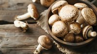 Fresh brown mushrooms in rustic wooden bowl on dark table, moody food photography with natural lighting and selective focus for culinary design.