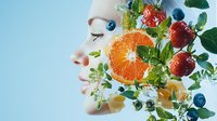 Young woman profile with fresh fruits and green leaves in double exposure effect against blue background, closed eyes expressing wellness and natural beauty.