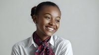 Young African American woman with bright smile wearing white button-up shirt and patterned scarf against neutral background, perfect for business or education marketing.