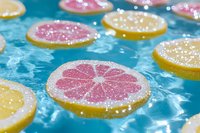 Fresh citrus slices floating in clear blue water with sparkling sugar crystals on top, creating refreshing summer mood for food and beverage concepts.