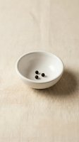 White ceramic bowl with black peppercorns on neutral linen fabric background for culinary and kitchen design projects.
