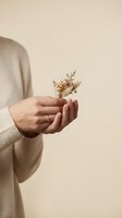 Woman hands gently holding delicate dried flowers in neutral beige sweater against warm minimalist background for wellness and mindfulness concepts.