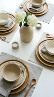 Elegant table setting with neutral ceramic dinnerware, wooden chargers, linen napkins and white hydrangea centerpiece for dining room decor.