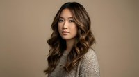 Young Asian woman with long wavy brown hair wearing beige knit sweater against neutral background. Professional portrait for fashion and lifestyle content.