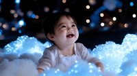 Young Asian toddler lying on soft white material with magical blue bokeh lights creating dreamy atmosphere, expressing pure joy and wonder with genuine laughter.