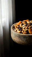 Mixed nuts and dried fruits in rustic wooden bowl on dark background. Healthy snacking, organic food ingredients for cooking and baking recipes.
