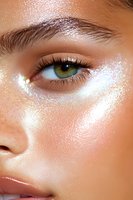 Close-up of glowing skin with shimmering highlighter makeup effect and green eye. Natural dewy complexion enhanced with pearlescent cosmetic products.