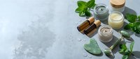 Natural organic skincare products with green herbs and cosmetic containers on marble surface for beauty wellness routine.