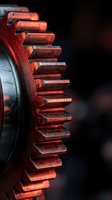 Close-up of red metal gear wheel with sharp teeth against dark background, industrial machinery component for engineering and manufacturing concepts.