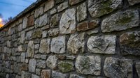 Ancient weathered stone wall with moss-covered blocks stretching into distance under dramatic sky. Historic masonry construction background texture.