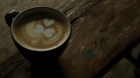 Artisanal cappuccino with heart-shaped latte art in dark ceramic cup on rustic wooden table, creating cozy coffee shop atmosphere.