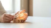 Business professional holding glowing lightbulb over ISO wooden blocks representing innovation and international standards compliance in corporate environment.