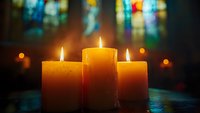 Three glowing candles against stained glass windows create peaceful atmosphere with warm candlelight and bokeh effect in church or spiritual setting.