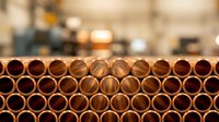 Stack of copper pipes arranged in rows with blurred industrial warehouse background. Construction materials for plumbing and heating systems installation.
