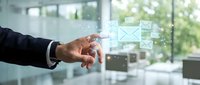 Businessman in dark suit touching digital email icon interface on transparent screen in modern office with window view, representing digital communication and business technology.