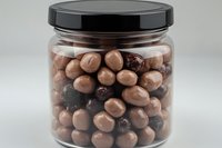 Glass jar filled with milk chocolate covered nuts and raisins against neutral background, appetizing snack mix ready for packaging and retail display.