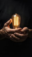 Hands gently holding glowing vintage Edison bulb with warm filament against dark background symbolizing innovation creativity and bright ideas.