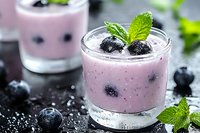 Fresh blueberry smoothie with mint garnish in glass, healthy breakfast drink with scattered berries and chia seeds on rustic wooden table surface.