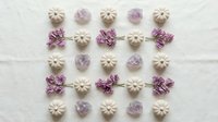 Flat lay arrangement of purple and white decorative elements including bows, buttons and ornamental shapes on light textured background for crafting projects.